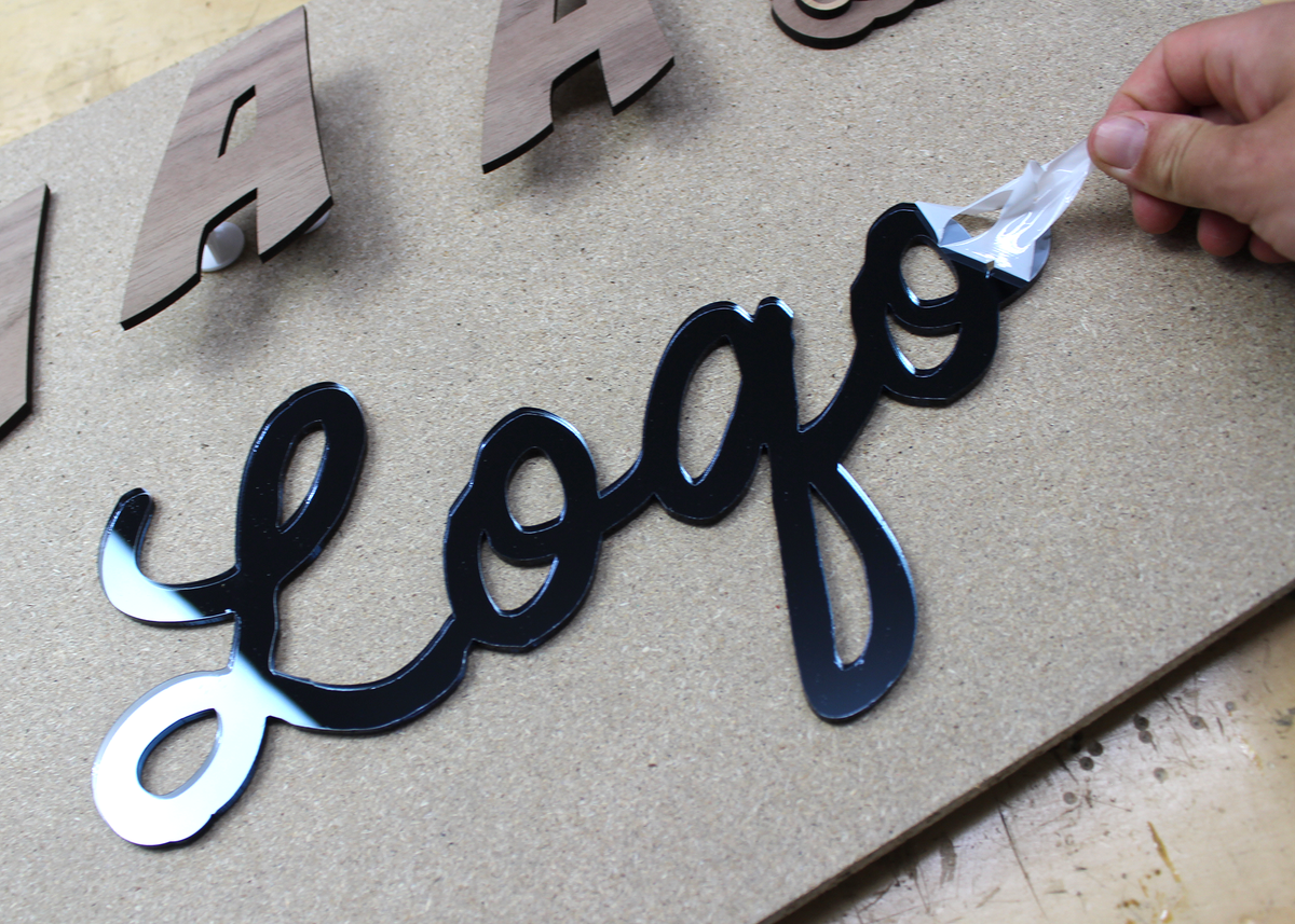 Beschermfolie wordt verwijderd van een lasergesneden logo uit antraciet spiegel acrylaat